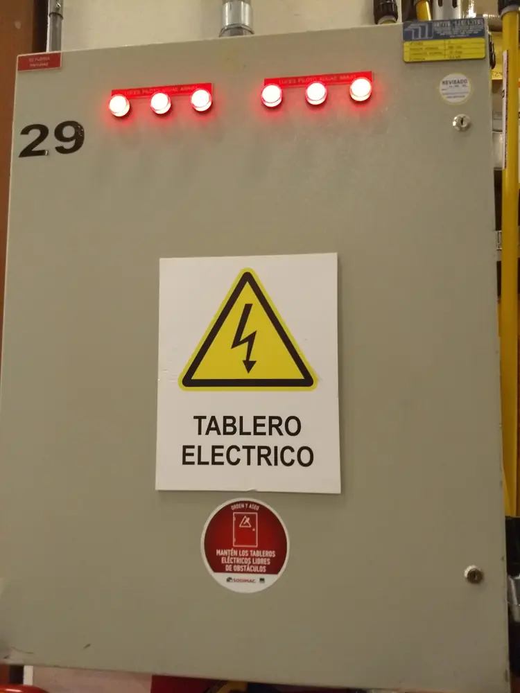 Puerta de tablero eléctrico de un local con señalética de riesgo eléctrico y luces piloto