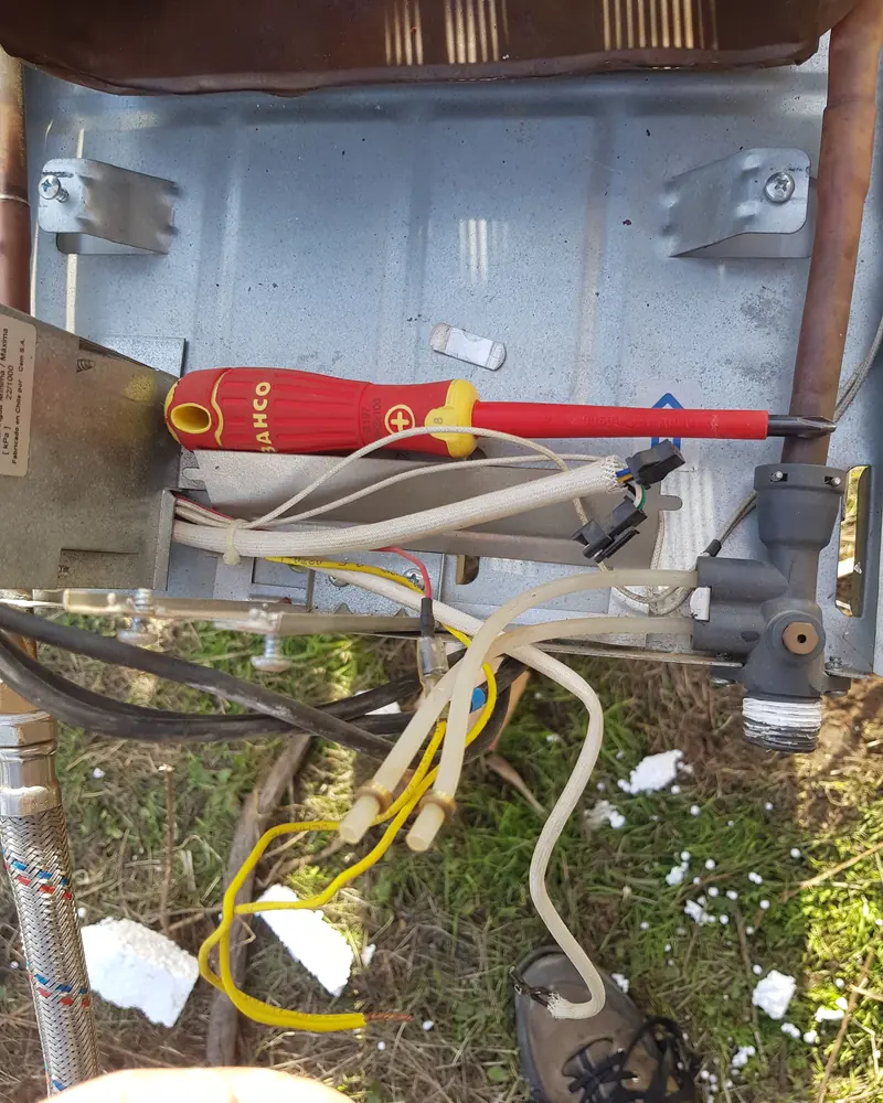 Interior de un calefont con cables y herramientas durante una revisión