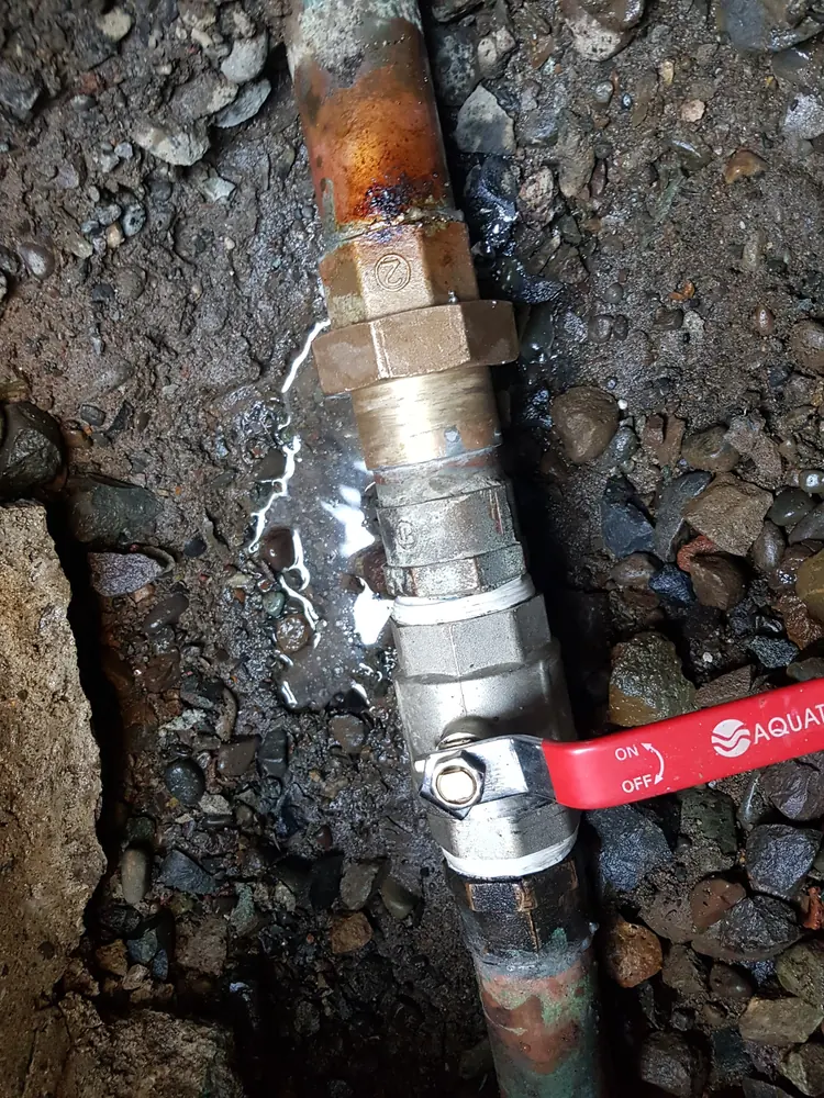 Llave de paso de bola con manilla roja en una cañería enterrada