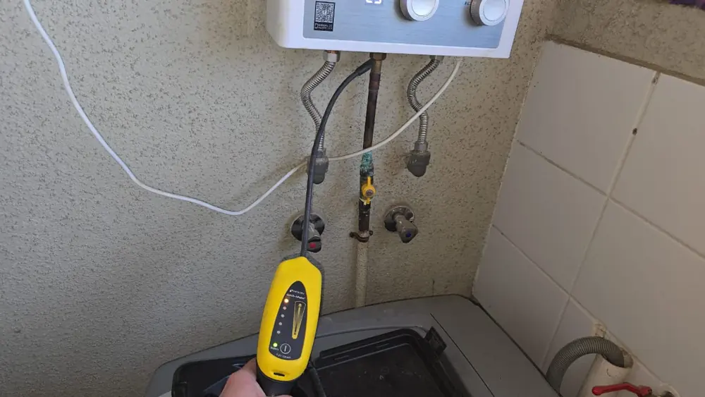 Detector electrónico amarillo revisando las conexiones de gas bajo un calefont